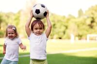 Toddlers Friends Playing: Boy Standing at Football Field Holding Soccer Ball Above Head while Smiling Girl is Sneaking from Behind Stock Photo - Image of child, happy: 186280202