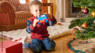 Happy little boy looking and smiling at toy train he got on Christmas. Child recieving presents on New Year Stock Photo | Adobe Stock