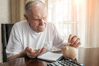 old man in the pandemic counts pennies from the pension fund. Concerned about lockdown, an elderly man puts money in a piggy bank. pensioner calculates the budget of his pension Stock Photo |