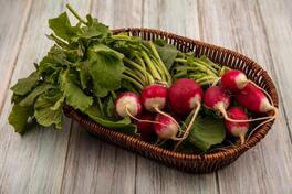 Free photo top view of crunchy root vegetable radishes on a bucket with leaves on a grey wooden surface